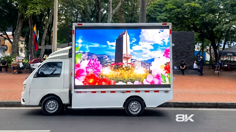 Carro valla LED con contenido de flores y ciudad frente a un parque