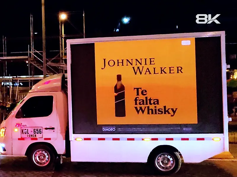 Carro valla con pantalla LED mostrando publicidad de una marca de whisky de noche