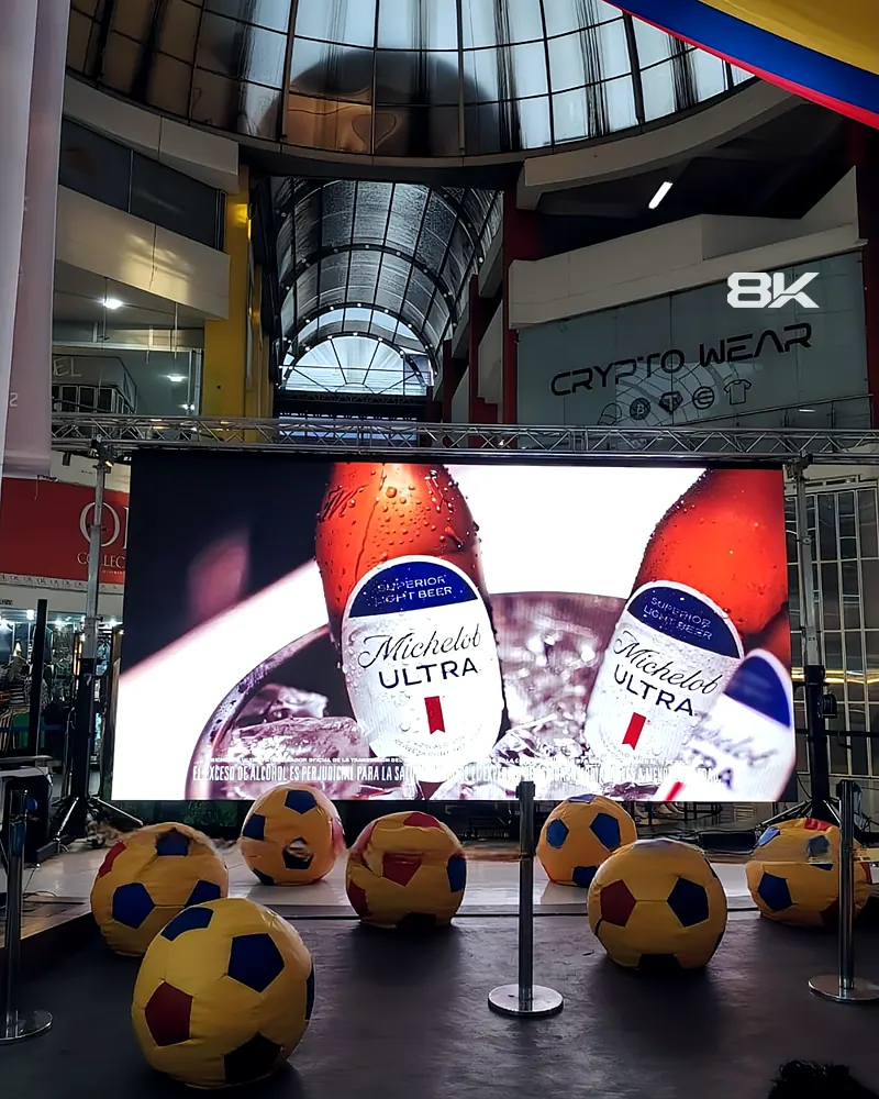 Pantalla LED en truss dentro de un centro comercial con publicidad de cerveza y puffs de balón
