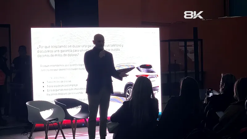 Conferencista frente a una pantalla LED en un salón con público