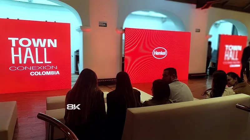 Town hall corporativo con pantalla LED central y pantallas verticales tipo tótem en rojo